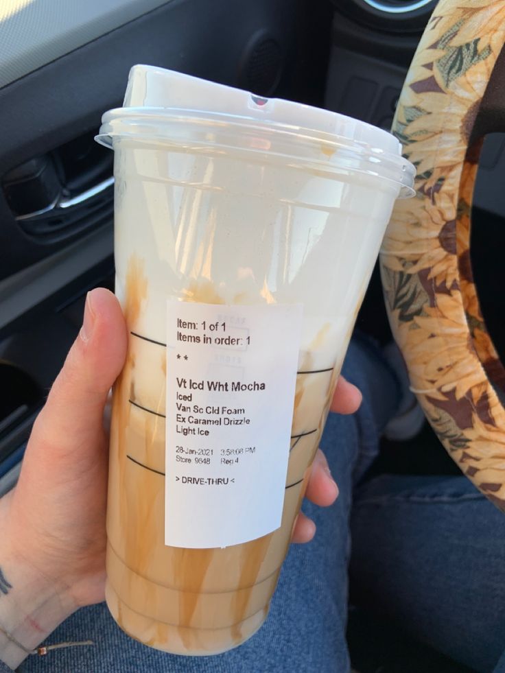 a person holding up a plastic cup with information on the side in their hand and steering wheel behind them