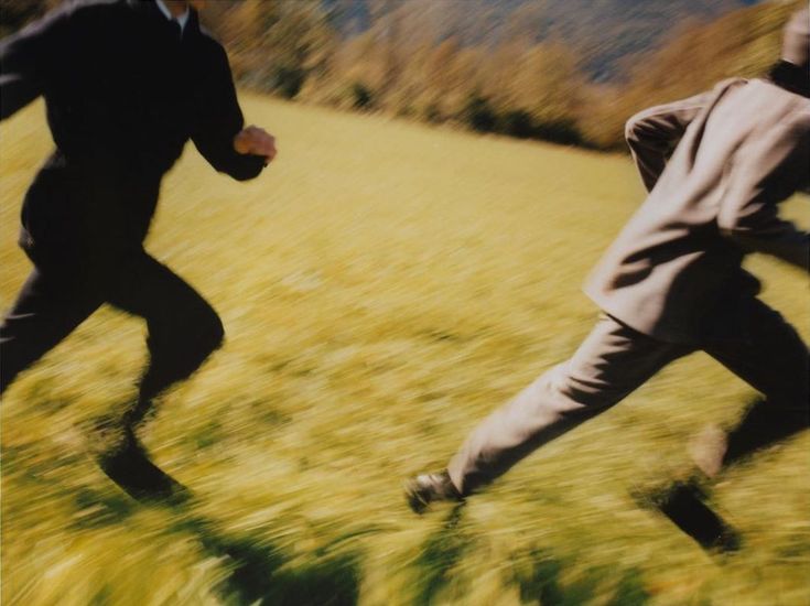 two men in suits are running through the grass