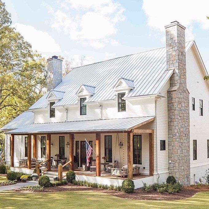 a white house with a metal roof and two story windows on the front, surrounded by greenery