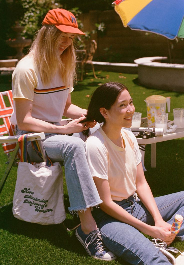 two women sitting on the grass in front of an umbrella