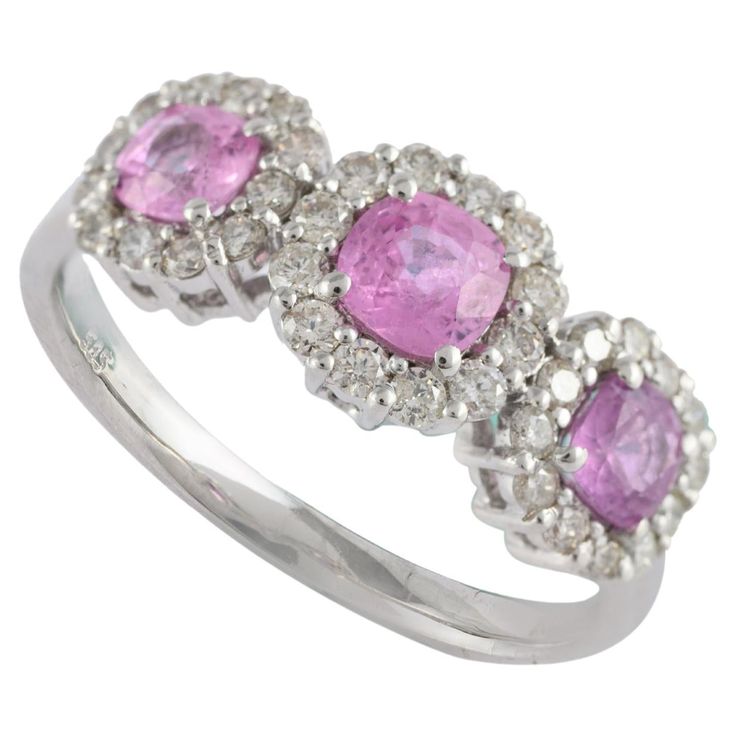 Pink Sapphire Three Stone Engagement Ring with Halo Diamonds Set in 14K Gold featuring natural pink sapphire of 0.9 carats and diamonds of 0.41 carat. The gorgeous handcrafted ring goes with every style. Sapphire stimulate concentration and reduces stress. Designed with three round cut pink sapphire, each surrounded with diamonds that makes it a perfect fit to wear it on your wedding or style it with any of your basic outfit to give it a glam. This is a great piece of jewelry to gift anyone on y White Gold Pink Sapphire Diamond Ring With Accents, Silver Diamond Ring With Halo Setting And Pink Sapphire, Pink Sapphire Three-stone Jewelry, White Gold Pink Sapphire Ring With Halo Setting, White Gold Brilliant Cut Pink Sapphire Jewelry, Gold Gemstone Ring, Three Stone Engagement, Handcrafted Rings, Three Stone Engagement Rings