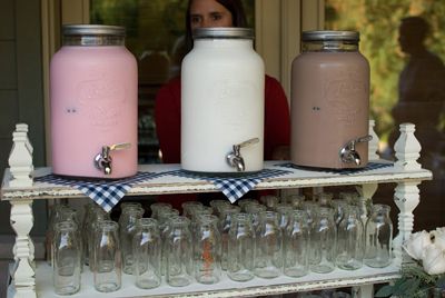 three jars are sitting on top of a shelf with glasses in front of them and a woman looking out the window