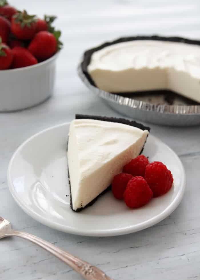 a slice of cheesecake with raspberries on a white plate next to a bowl of strawberries