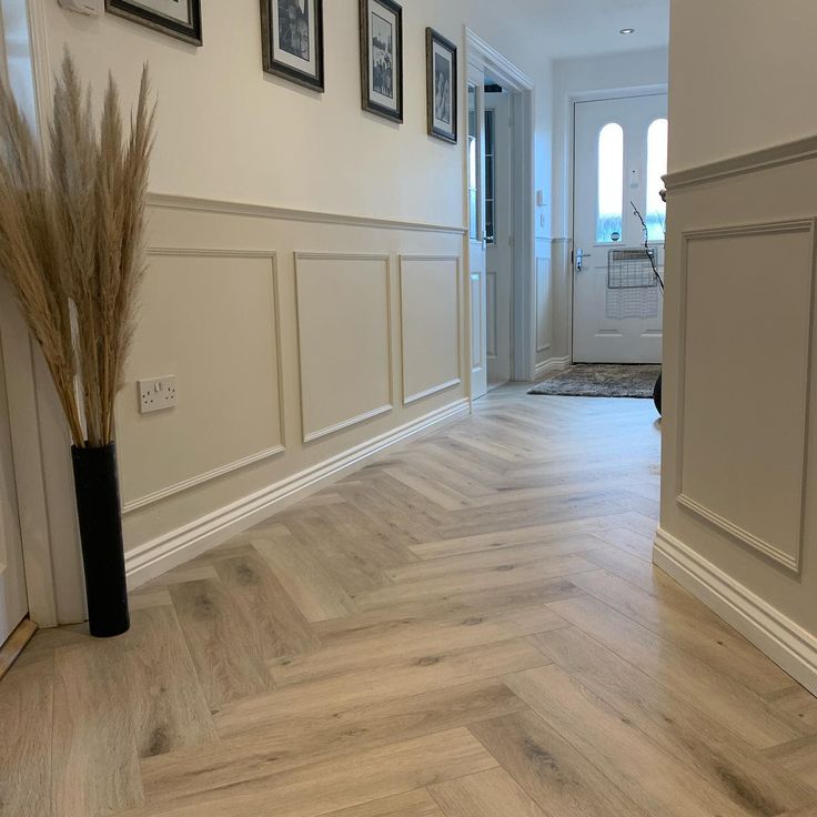 an empty hallway with white walls and wood flooring on the side, along with framed pictures