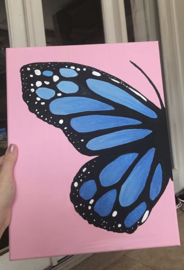 a hand holding up a blue and black butterfly on a pink background with white dots