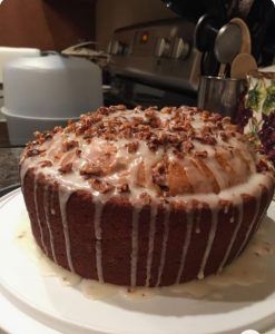 a cake sitting on top of a white plate covered in frosting and nuts next to a coffee pot