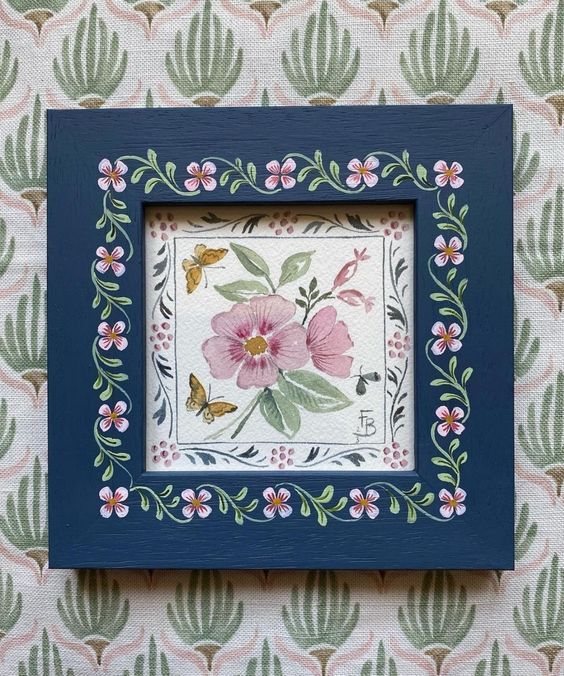 a blue frame with pink flowers and green leaves on it, against a wallpapered background