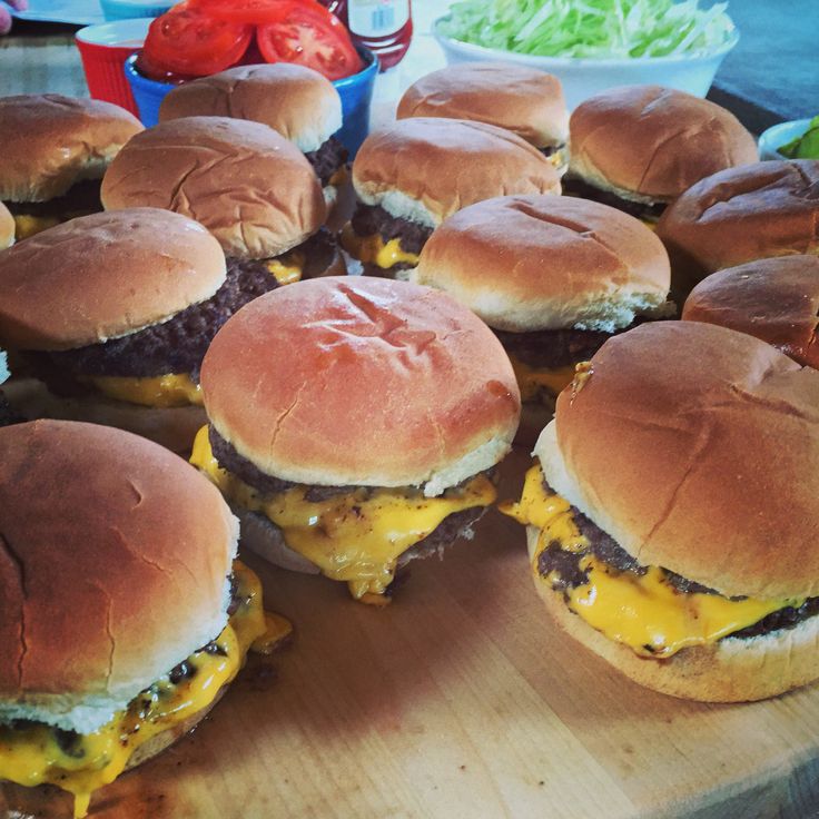 several cheeseburgers are arranged on a cutting board