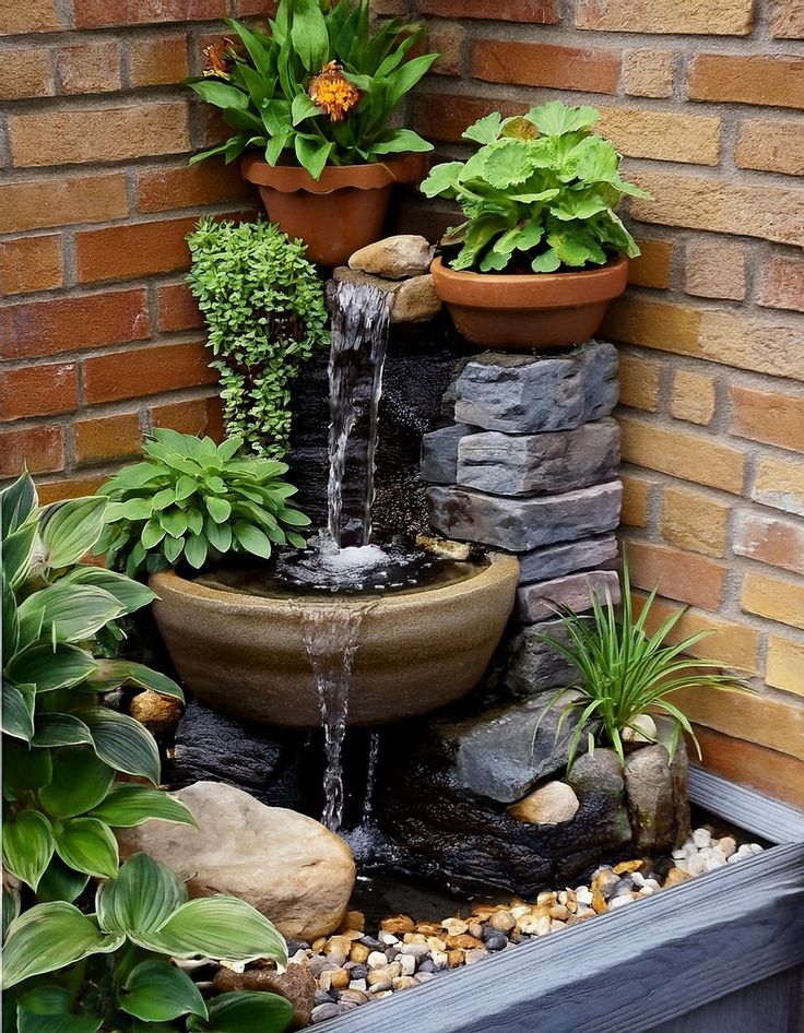 a water fountain surrounded by potted plants and rocks in front of a brick wall