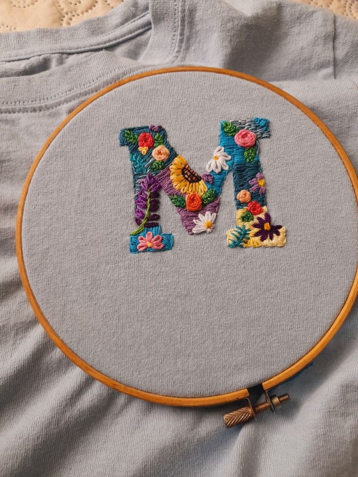 the letter m is made up of colorful flowers and has a wooden hoop hanging from it