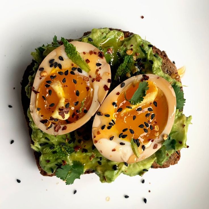 an open face sandwich topped with avocado and hard boiled eggs, garnished with black sesame seeds