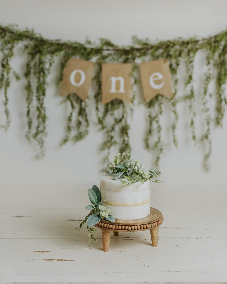 a white cake sitting on top of a wooden table next to a sign that says one