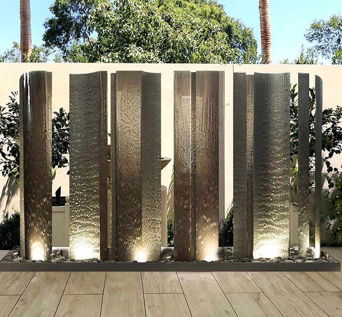 an outdoor fountain with lights on in front of a wall and trees behind the fence