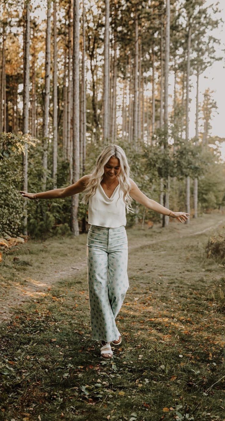 a woman is walking through the woods with her arms outstretched