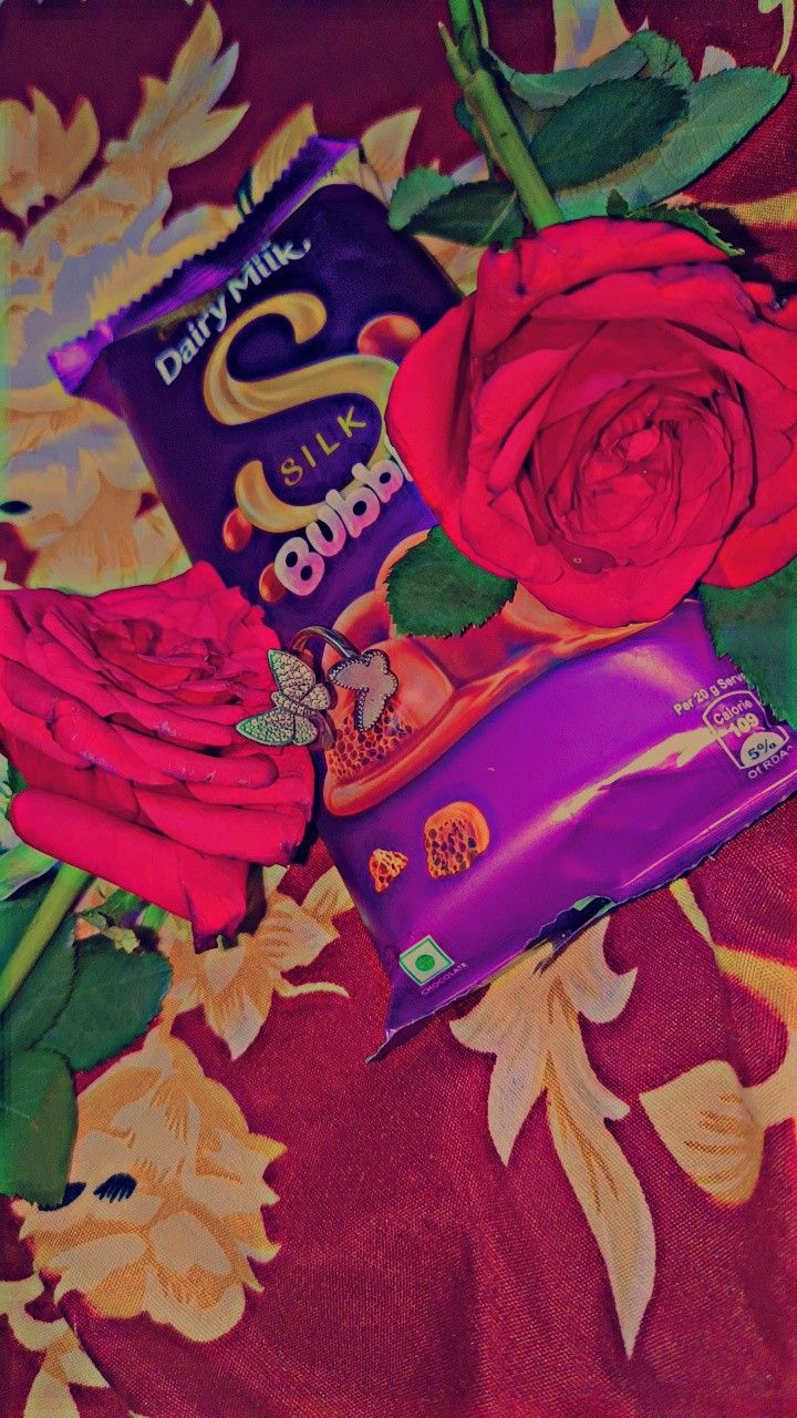 a chocolate bar sitting on top of a bed next to red roses and a flower