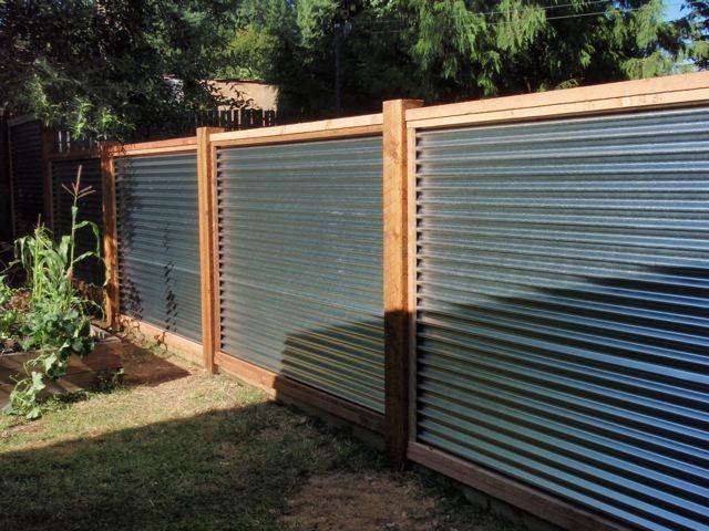 a fence that is made out of metal sheets and wood slats, in the backyard