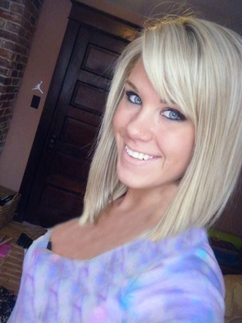 a woman with long blonde hair and blue eyes smiles at the camera while standing in front of a brick wall