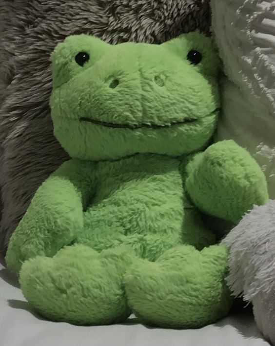 a green frog stuffed animal sitting on top of a bed