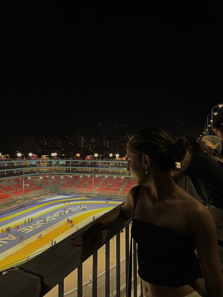 a woman is looking out over an ice rink at night with people on the sidelines