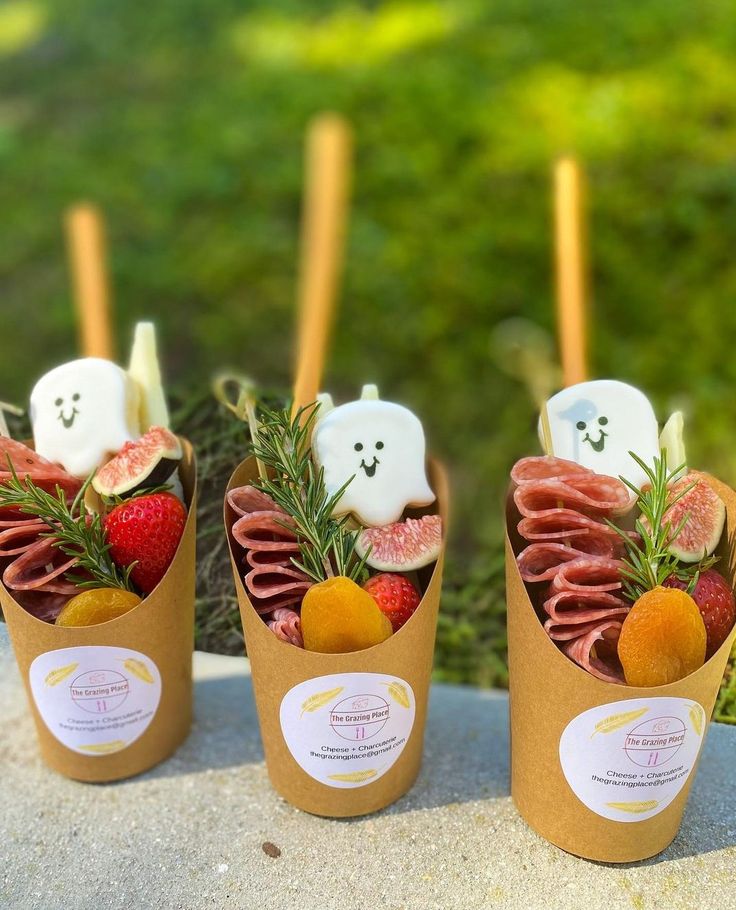 three small cups filled with food on top of a cement slab next to grass and trees