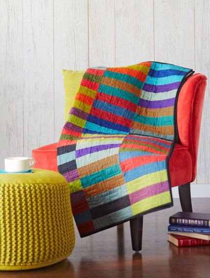 a brightly colored chair and footstool in front of a white wall with books on the floor