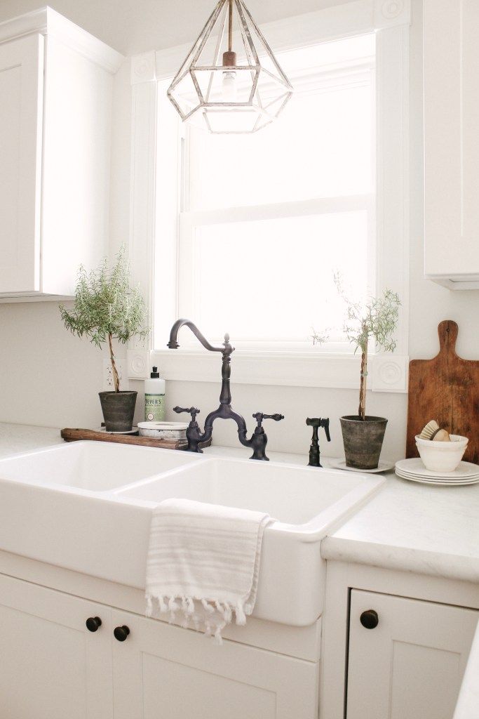 a white kitchen sink sitting under a window next to a faucet and potted plant