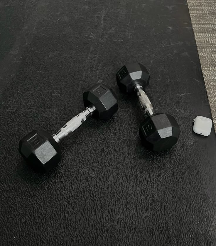 three black dumbbells sitting on the ground next to a white and gray object