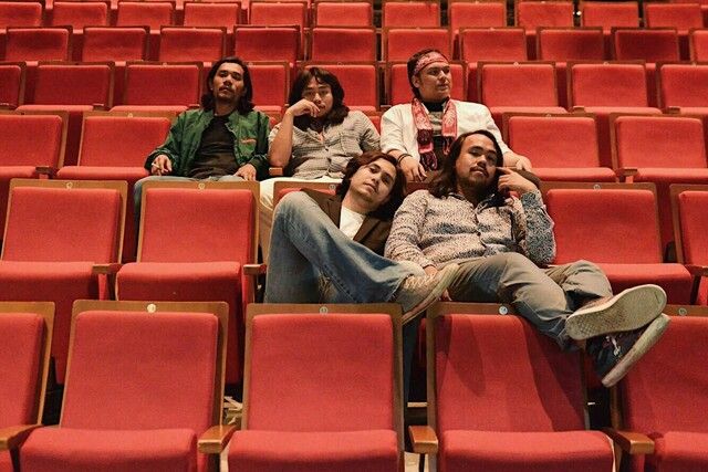 four people sitting in an auditorium with red seats