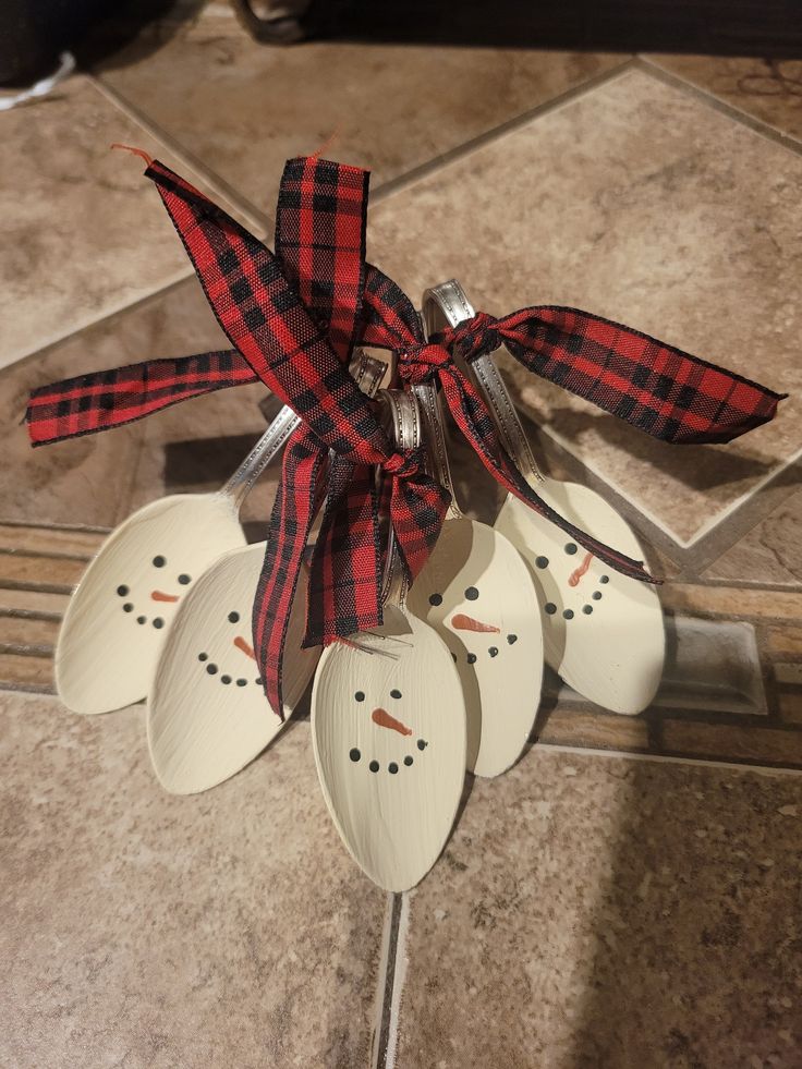 four spoons with snowmen on them are tied to a metal holder in the middle of a tile floor