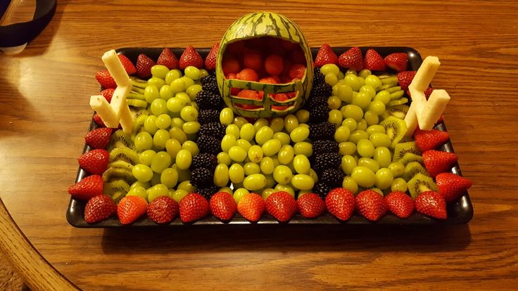 a fruit tray with grapes, strawberries, melons and bananas arranged in the shape of a football helmet