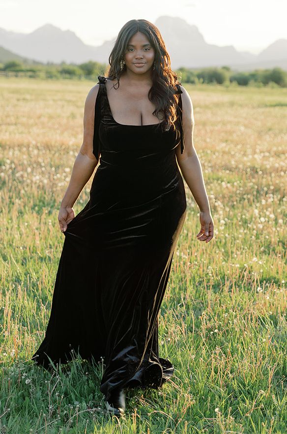 a woman in a long black dress is standing in the middle of a grassy field