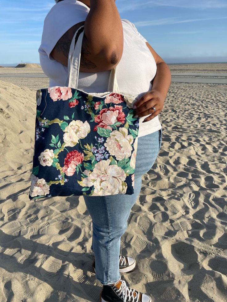 a woman is standing on the beach with her hand in her pocket and she has a large floral tote bag