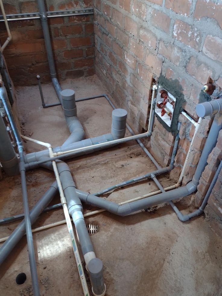 pipes and piping in an unfinished room next to a brick wall with exposed plumbing