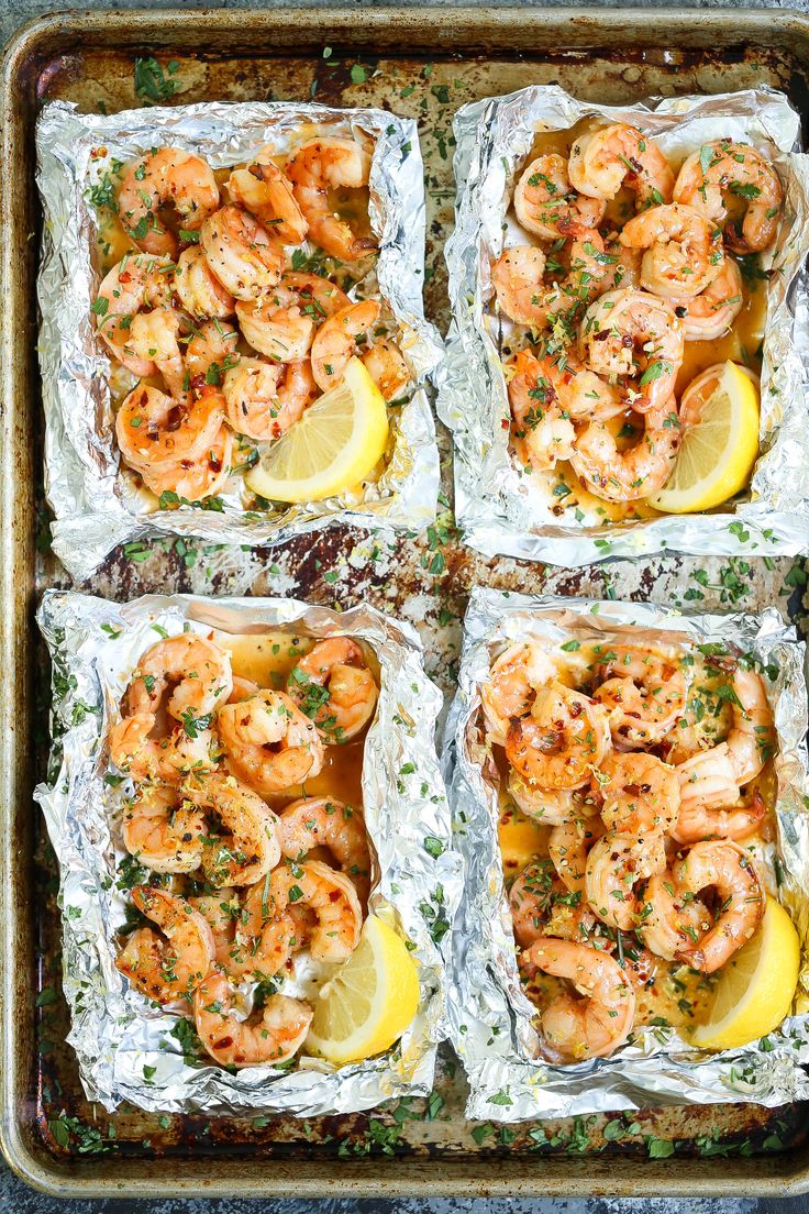 four square trays filled with shrimp and lemon on top of tin foil covered in parsley