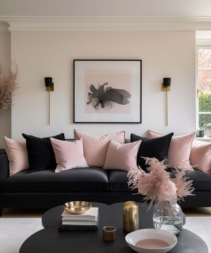 a living room with black couches, pink pillows and a coffee table in front of a window