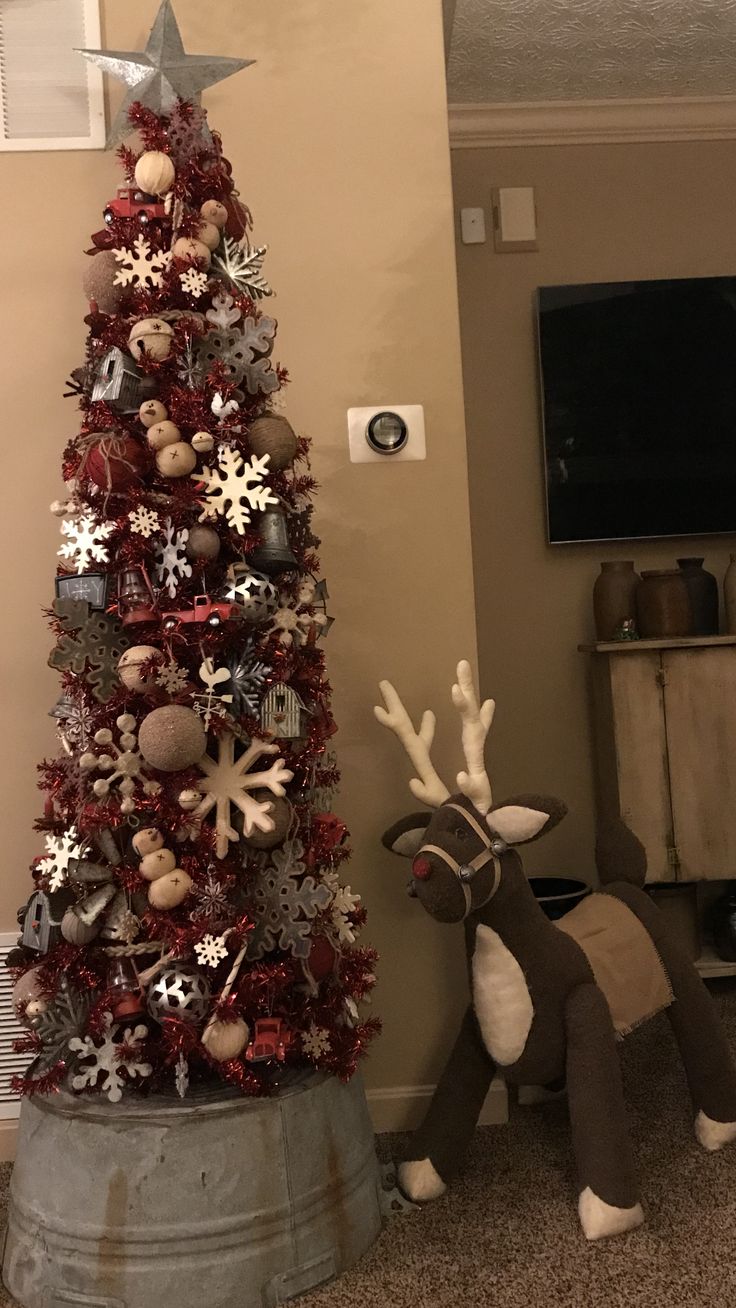 a christmas tree decorated with silver and red ornaments is next to a reindeer statue in a living room