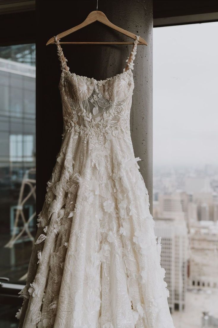 a wedding dress hanging on a window sill in front of a cityscape