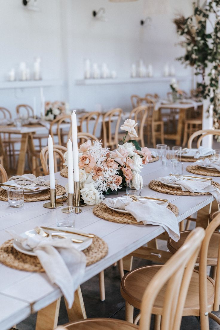 the table is set with place settings and flowers on it, along with candles for centerpieces