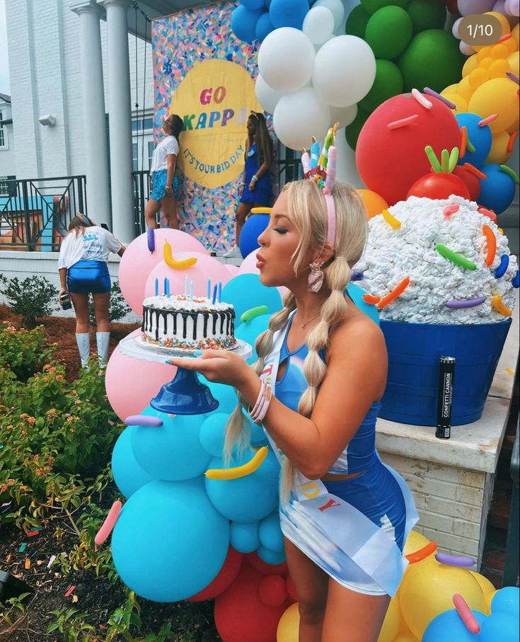 a woman holding a cake in front of balloons