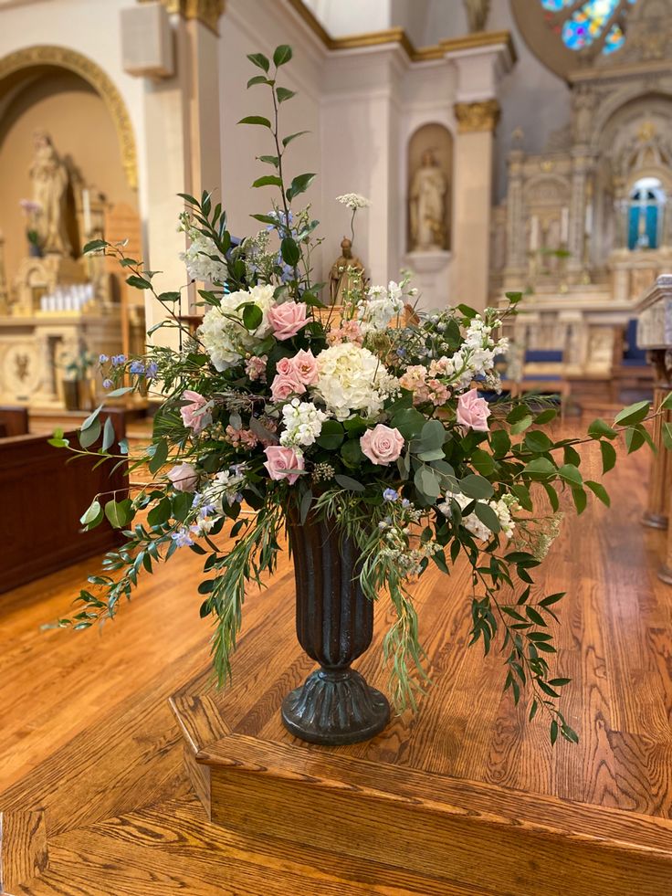 a vase filled with lots of flowers on top of a wooden table in a church