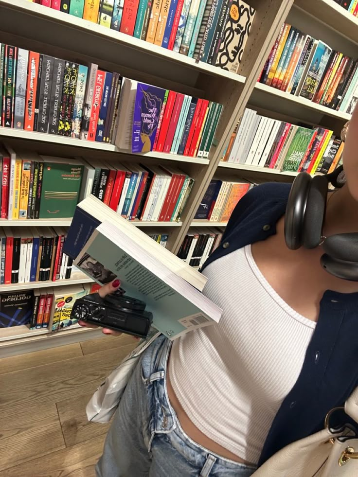 a woman wearing headphones reading a book in front of a library full of books