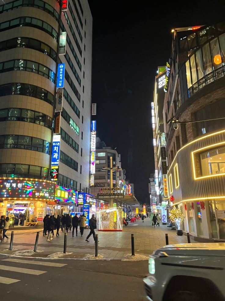 people are walking on the street in front of tall buildings at night with neon lights