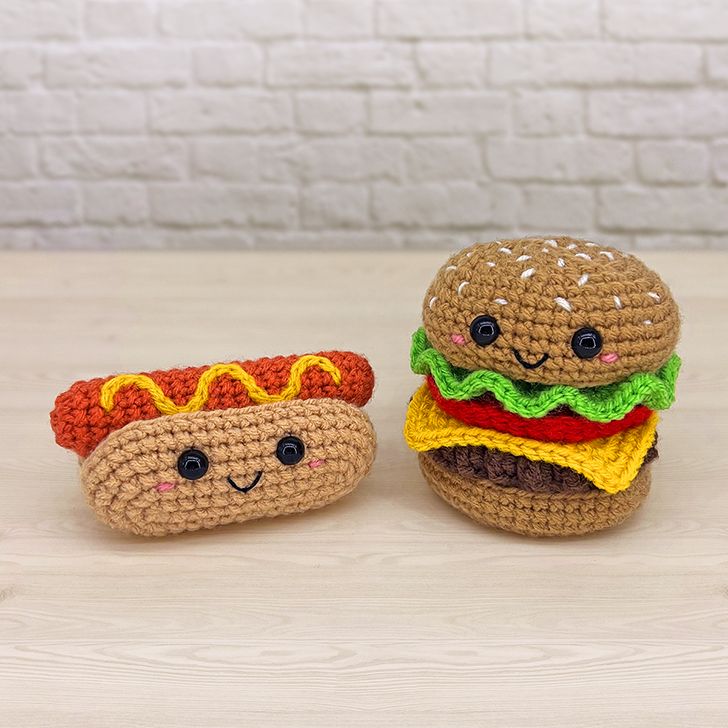 two crocheted hamburgers and a hot dog are sitting on a table next to each other