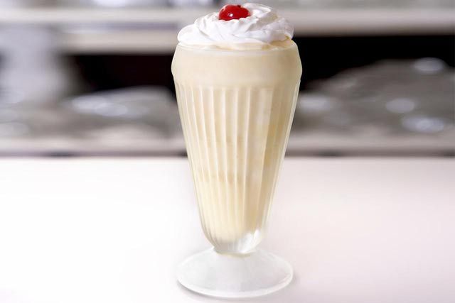 a tall glass filled with whipped cream and a cherry on the top is sitting on a table