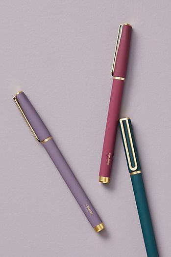 two pens sitting next to each other on top of a purple surface with gold trim