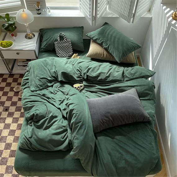 a bed with green sheets and pillows in a room next to a checkered floor