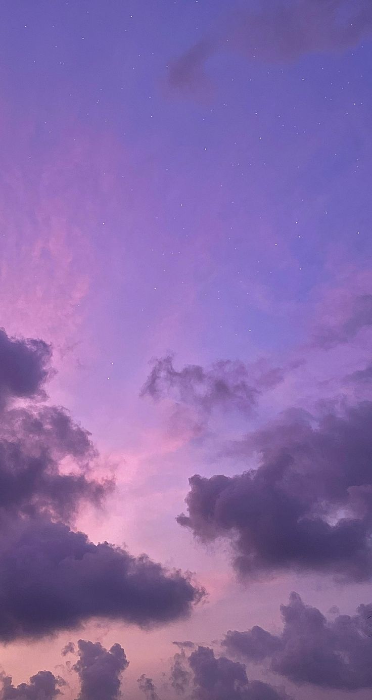 the sky is filled with purple clouds and stars in the distance, as seen from an airplane