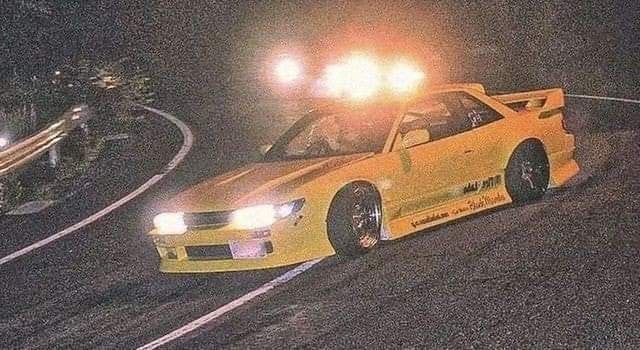 a yellow car driving down a road at night with lights on it's headlamps