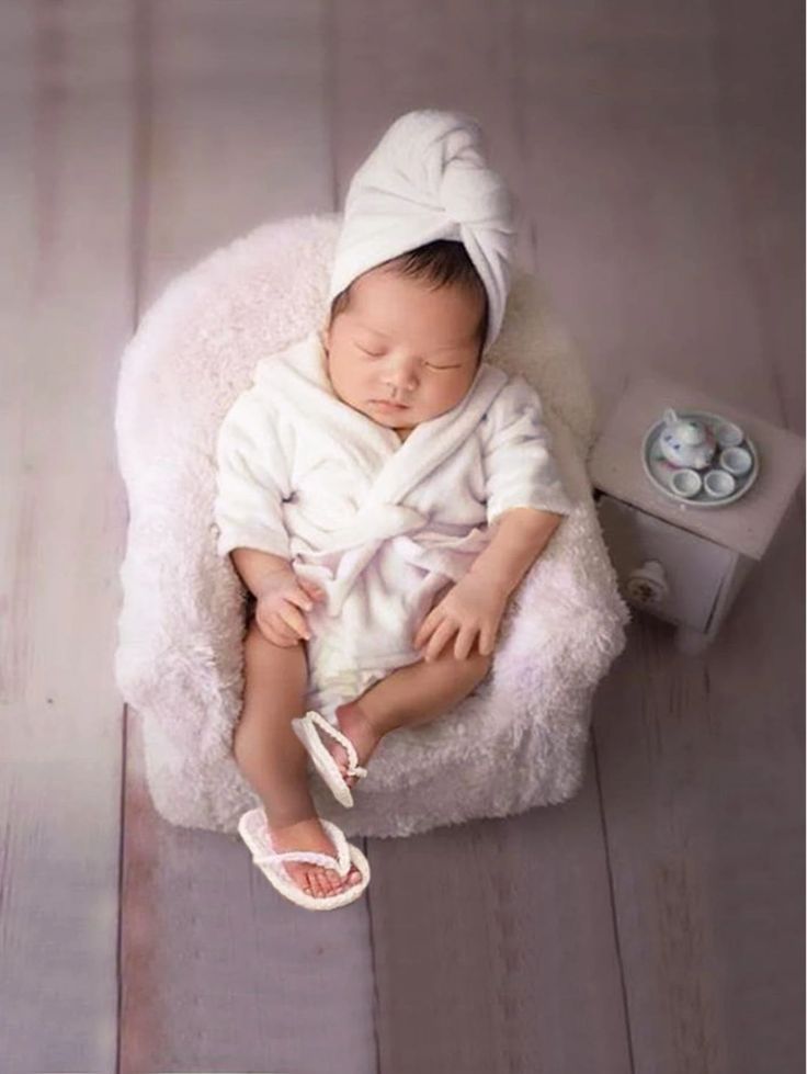 a baby in a white robe is laying down on a chair with a pair of shoes next to it