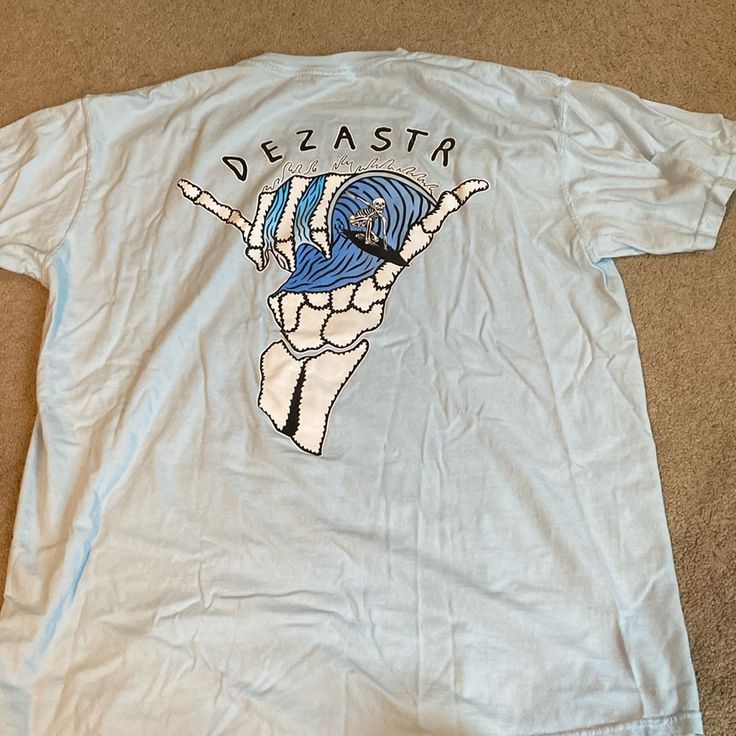 Baby Blue Surfing Skeleton Graph Tshirt. Brand Is Dezster. Size Xlarge. Never Worn. Perfect Condition. Light Blue Graphic T-shirt For Streetwear, Light Blue Screen Print T-shirt For Streetwear, Light Blue Graphic Print Top For Streetwear, Light Blue Graphic Top For Streetwear, Light Blue Graphic Tee With Graphic Print, Blue Crew Neck T-shirt With Back Print, Light Blue Graphic T-shirt, Blue Graphic Tee With Back Print, Blue Band Merch Top For Streetwear